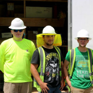 Three solar apprentices in high-visibility vests and white hard hats pose for the camera in southwest Virginia.