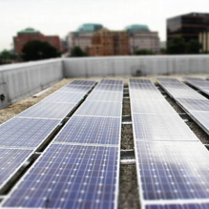 Rows of solar panels are pictured on the roof of a building in Arlington, Virginia. The city skyline is seen in the distance.