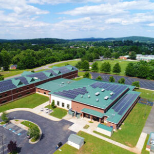 An aerial photo shows solar panels on the roof of Prospect Heights Middle School in Orange County, Virginia. The Blue Ridge Mountains are visible in the background.
