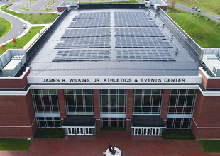 An overhead photo shows a large solar panel array on the roof of the James R. Wilkins Jr. Athletics and Events Center.