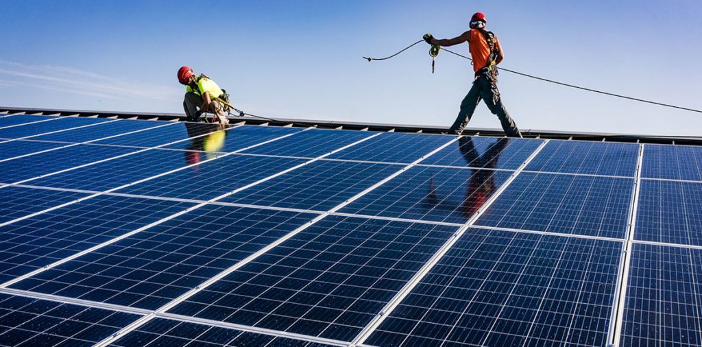 Two men wearing hard hats install a solar panel