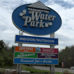 A large roadside sign for Massanutten Water Park. The primary sign is blue and oval shaped, and smaller, rectangular signs and stacked below it to advertise features in the park.
