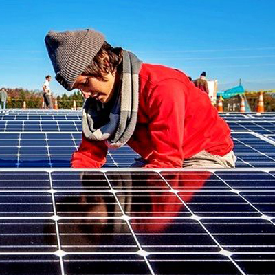 A man wearing a beanie and a red jacket installs a solar panel.