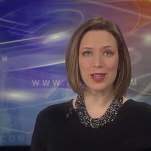 A female news anchor with brown hair wearing a dark blouse presents a TV broadcast.