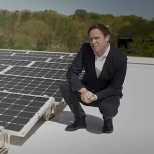 Sky News presenter Ed Conway stands next to a rooftop solar array in Richmond, Virginia.