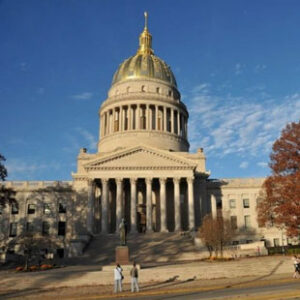 A photo of the West Virginia capitol building. Two people are walking towards the entrance.