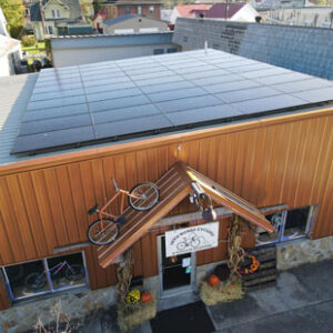 A photo of the entrance to a cycling shop in Big Stone Gap, Virginia. Solar panels cover the roof and an orange bicycle is perched above the entryway.