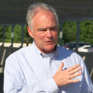 Senator Tim Kaine, wearing a light blue shirt, speaks to the press at a solar panel canopy on the campus of Washington & Lee University in Lexington, Virginia.